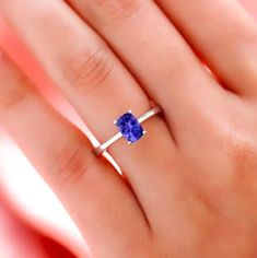 a woman's hand holding a ring with a blue stone in the middle and a thin band around it