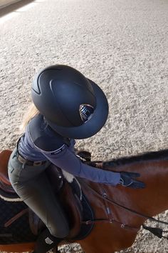 a woman riding on the back of a brown horse next to a person wearing a helmet