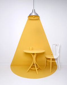 two chairs and a table in front of a yellow triangle shaped wall with a light hanging over it