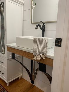 a white sink sitting under a bathroom mirror next to a wooden counter top with a black faucet