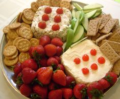 a platter with crackers, strawberries, cucumbers and cheese