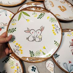 a person is holding a plate with an image of a bunny on it, surrounded by other plates and spoons