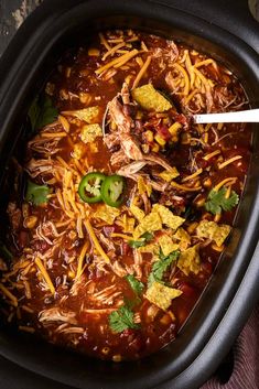 a crock pot filled with chili, corn and tortilla bread topped with shredded cheese