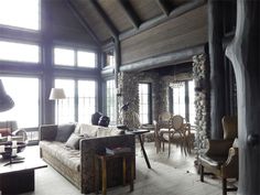 a living room filled with lots of furniture and windows next to a stone wall covered in logs