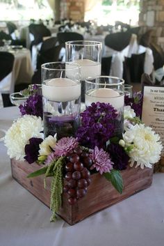 a wooden box filled with lots of flowers and candles on top of a white table cloth