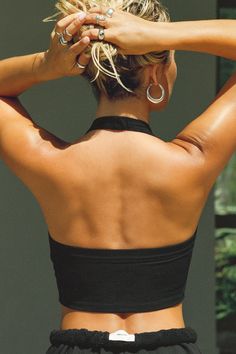 the back of a woman's black top with her hands on her head and one hand in her hair