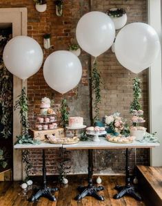 a table topped with lots of white balloons next to cakes and cupcakes on top of wooden tables