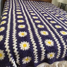 a crocheted granny blanket with daisies on the edge is displayed in front of a bed