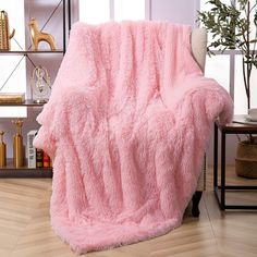 a pink blanket sitting on top of a wooden floor next to a white chair in a living room