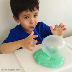 a young boy sitting at a table with a toothbrush in his mouth while blowing bubbles