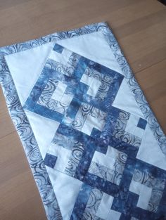 a blue and white quilted table runner on top of a wooden floor next to a black cat