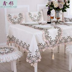 a dining room table set with white chairs and a vase full of flowers on it