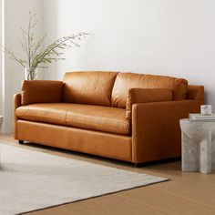 a brown leather couch sitting on top of a wooden floor next to a white wall