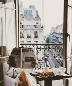 a person sitting in a chair reading a newspaper while holding a cell phone and looking at the eiffel tower