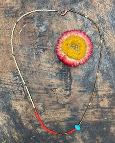 a red and yellow flower is on a wooden surface next to a beaded necklace