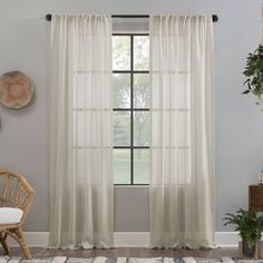 a living room with white curtains and a chair in front of the window that has a potted plant next to it