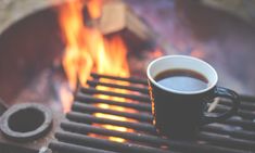 a cup of coffee sitting on top of a table next to a fire place with flames in the background