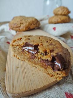 two chocolate chip cookies sitting on top of a wooden cutting board next to each other