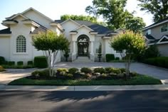 a large white house with lots of trees and bushes around it's front entrance