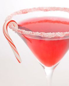 a candy cane is sticking out of the rim of a pink cocktail glass with red liquid