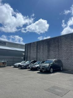 several cars parked in a parking lot next to a building with a large brick wall