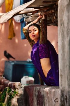 a woman in purple is leaning on the wall with her hands behind her head and looking off into the distance