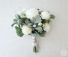 a bridal bouquet with white flowers and greenery on a wall in the background