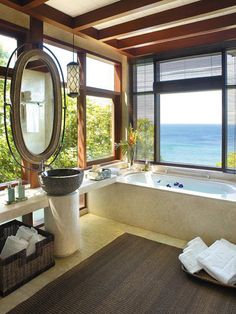 a large bath tub sitting under a window next to a sink in a bathroom near the ocean