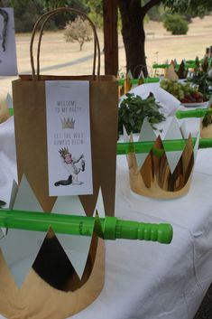 a table topped with paper bags and green straws next to plants on top of white cloth covered tables