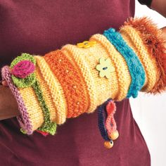 a person wearing a colorful knitted arm warmer with flowers on the cuff and buttons