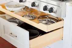 an open drawer with pots and pans on it in front of a stove top oven