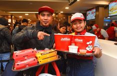 two young men holding trays of food at a fast food restaurant with people in the background