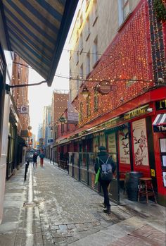 people are walking down the street in front of shops and buildings with christmas lights on them