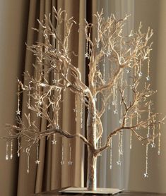 a white tree is sitting on a table in front of a window with drapes