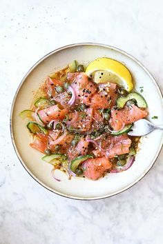 a white plate topped with salmon and cucumbers next to a lemon wedge on top of a table