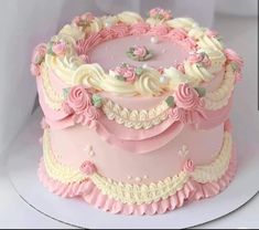 a pink cake with white frosting and flowers on it's top is sitting on a plate