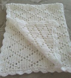 a white crocheted blanket laying on top of a bed next to a pillow