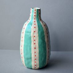 a green and white striped vase sitting on top of a gray table next to a wall