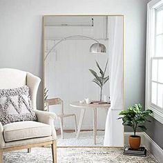 a living room with a chair, table and large mirror in front of the window