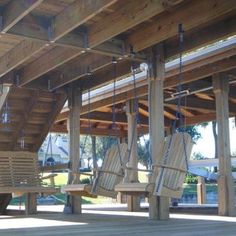 several wooden swings hanging from the roof of a covered area with wood posts and beams