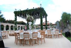 tables and chairs are set up for an outdoor wedding reception with greenery hanging from the ceiling