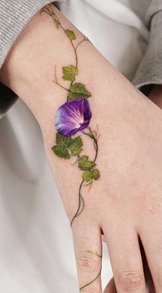 a woman's hand with a purple flower on it and green leaves attached to the wrist