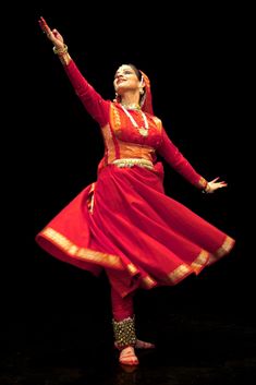 a woman in a red dress is dancing with her arms up and hands out to the side