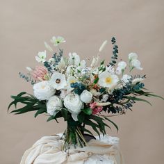 a vase filled with white and pink flowers on top of a wooden table next to a blanket