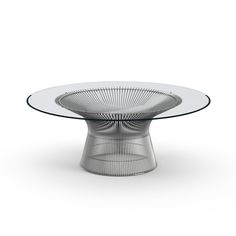 an oval glass table with metal legs and a circular design on the top, sitting in front of a white background