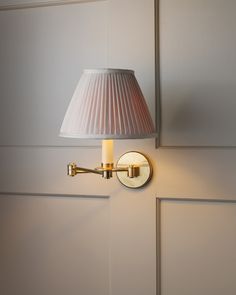 a wall light with a white shade on it's side and a mirror behind it