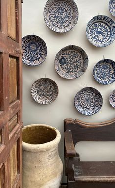 blue and white plates hanging on the wall next to a wooden bench with a planter