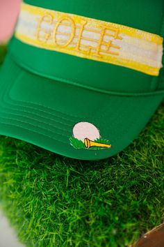 Get ready to tee off in style with the GOT GAME GOLF TRUCKER HAT. This green hat features a unique yellow striped ribbon and a gold Golf patch, adding a touch of flair to your golfing attire. Plus, the golf tee patch on the bill is a playful nod to your love for the game. Get ready to hit the course and turn heads with this quirky and fun hat. This is a made-to-order item. All customized orders are currently shipping within 14 business days. To receive item quicker, expedited shipping is availab Green Golf Cap, Green Baseball Cap For Golf, Fun Hat, Golf Tee, Green Hat, Got Game, Striped Ribbon, Golf Tees, Green Hats