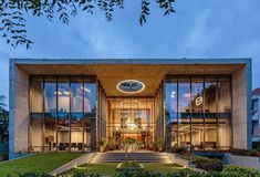 the entrance to a modern building with large windows and plants on the lawn at dusk