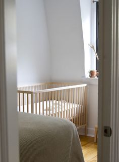 a baby crib in the corner of a room with white walls and wood floors